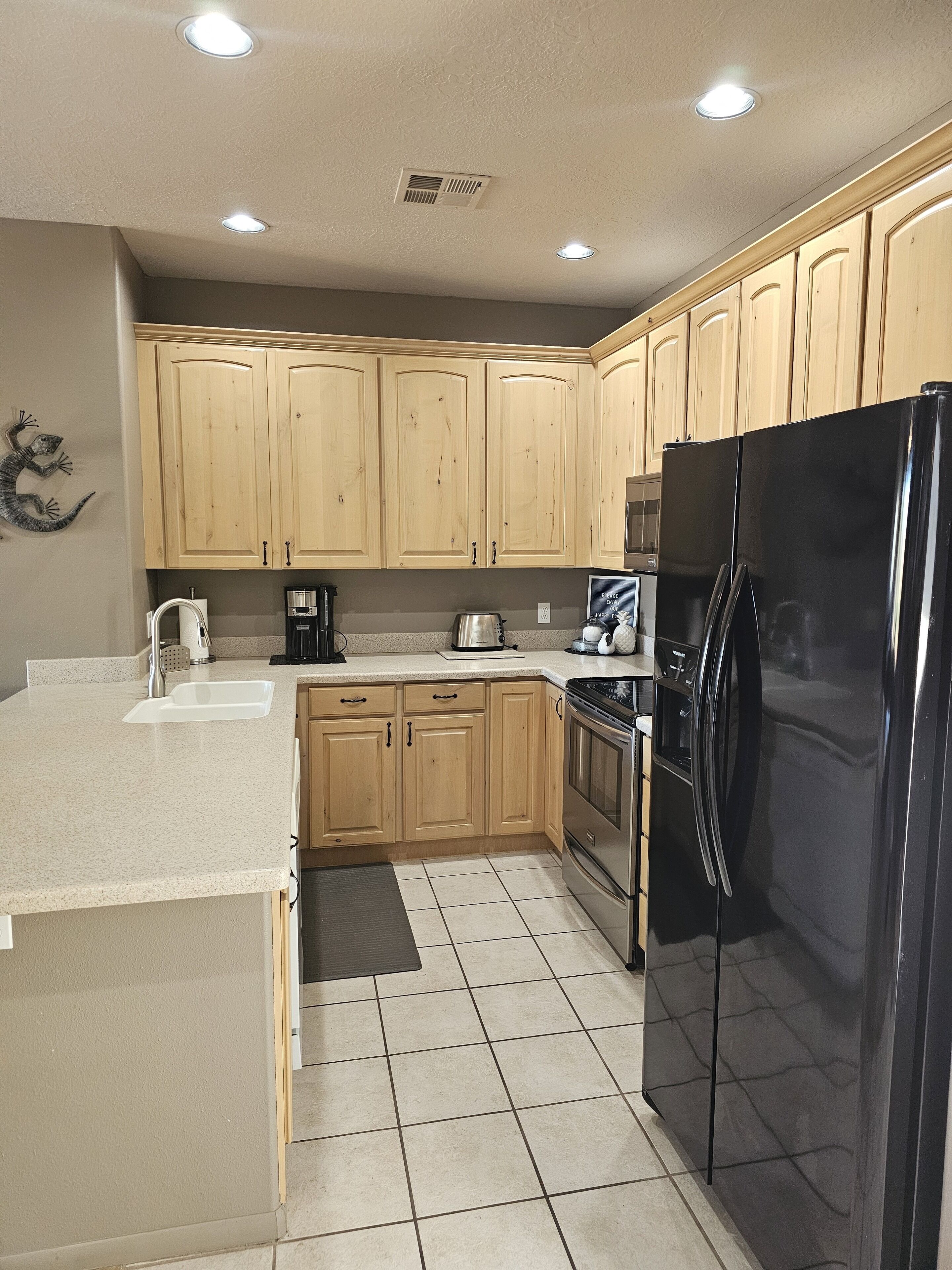 A kitchen with wooden cabinets, a black refrigerator, a coffee maker, and a dishwasher.