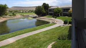 A residential area with a pond, a walking path, and a building with a flat roof. - Gated Golf Course Community Condo (St. George)