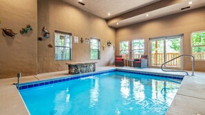 An indoor swimming pool with a stone wall, a small bar area, and multiple windows.