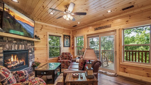 A cozy cabin interior with a stone fireplace, wooden walls, and large windows offering views of the outdoors.