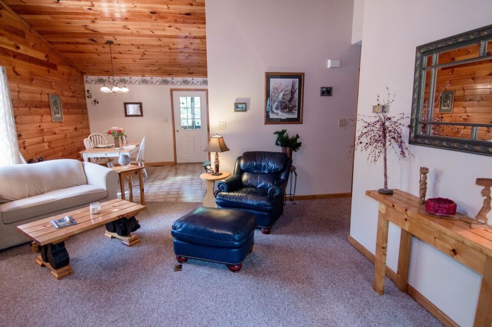 Una sala de estar acogedora con techo de madera, un sofá, una mesa de centro, un sillón de cuero y una mesita de madera con un jarrón.