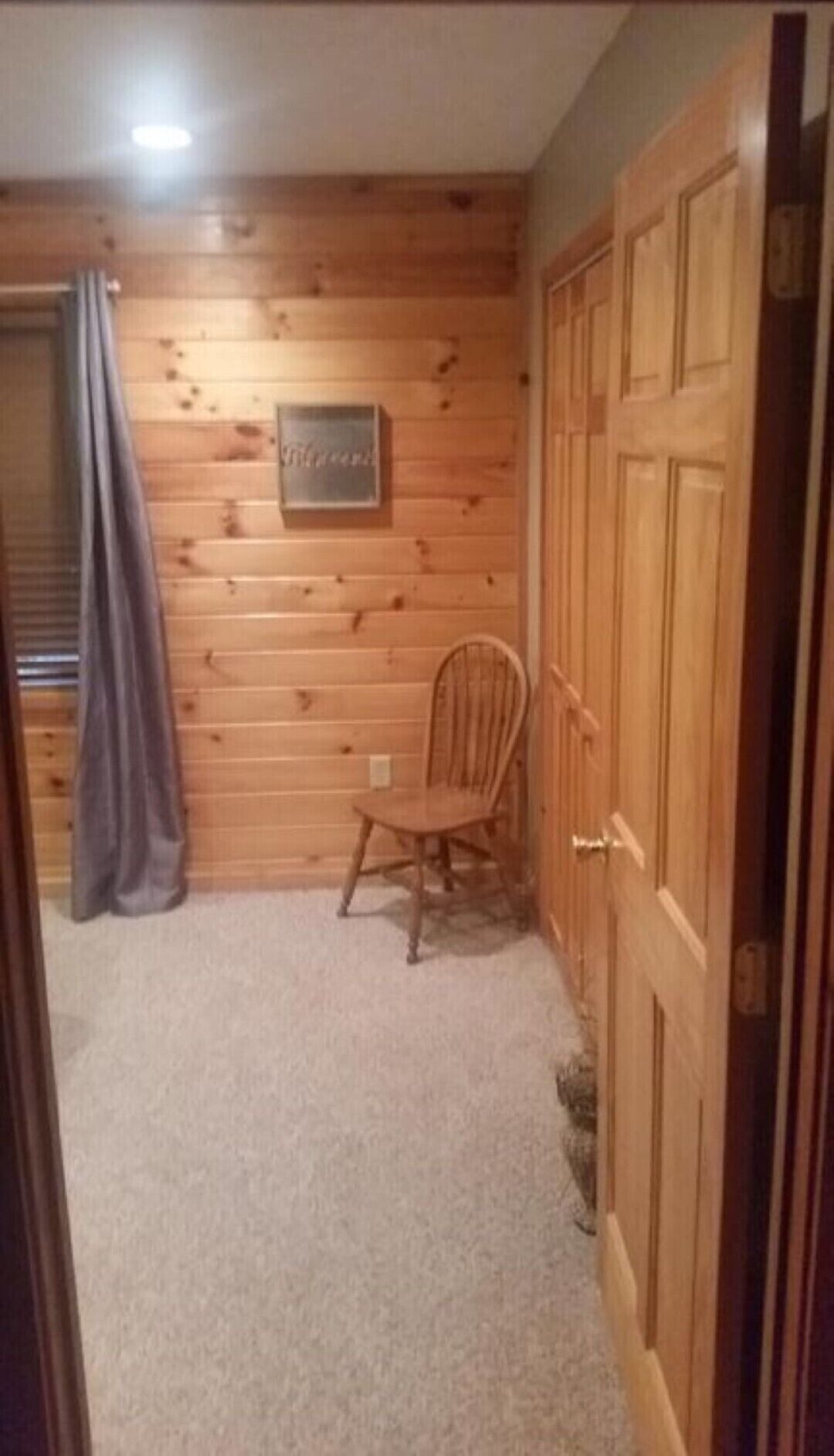 Una habitación con paneles de madera, una puerta de madera, una silla y suelo alfombrado.