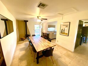 Uma sala de jantar com uma mesa e cadeiras de madeira, um ventilador de teto e um cartaz na parede.