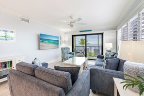 A modern living room with a large window, a ceiling fan, and a view of the ocean.
