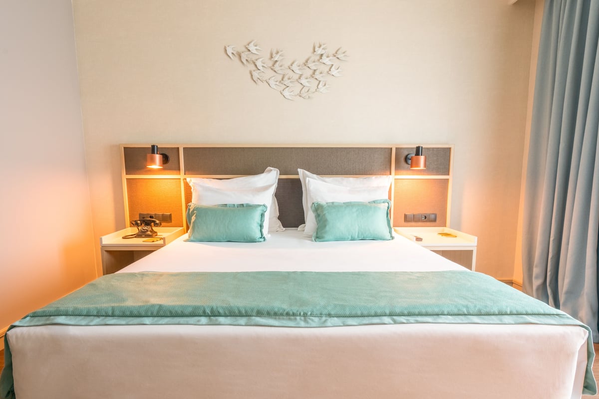 Une chambre d’hôtel avec un grand lit, deux tables de chevet, un luminaire fixé au mur et un rideau.