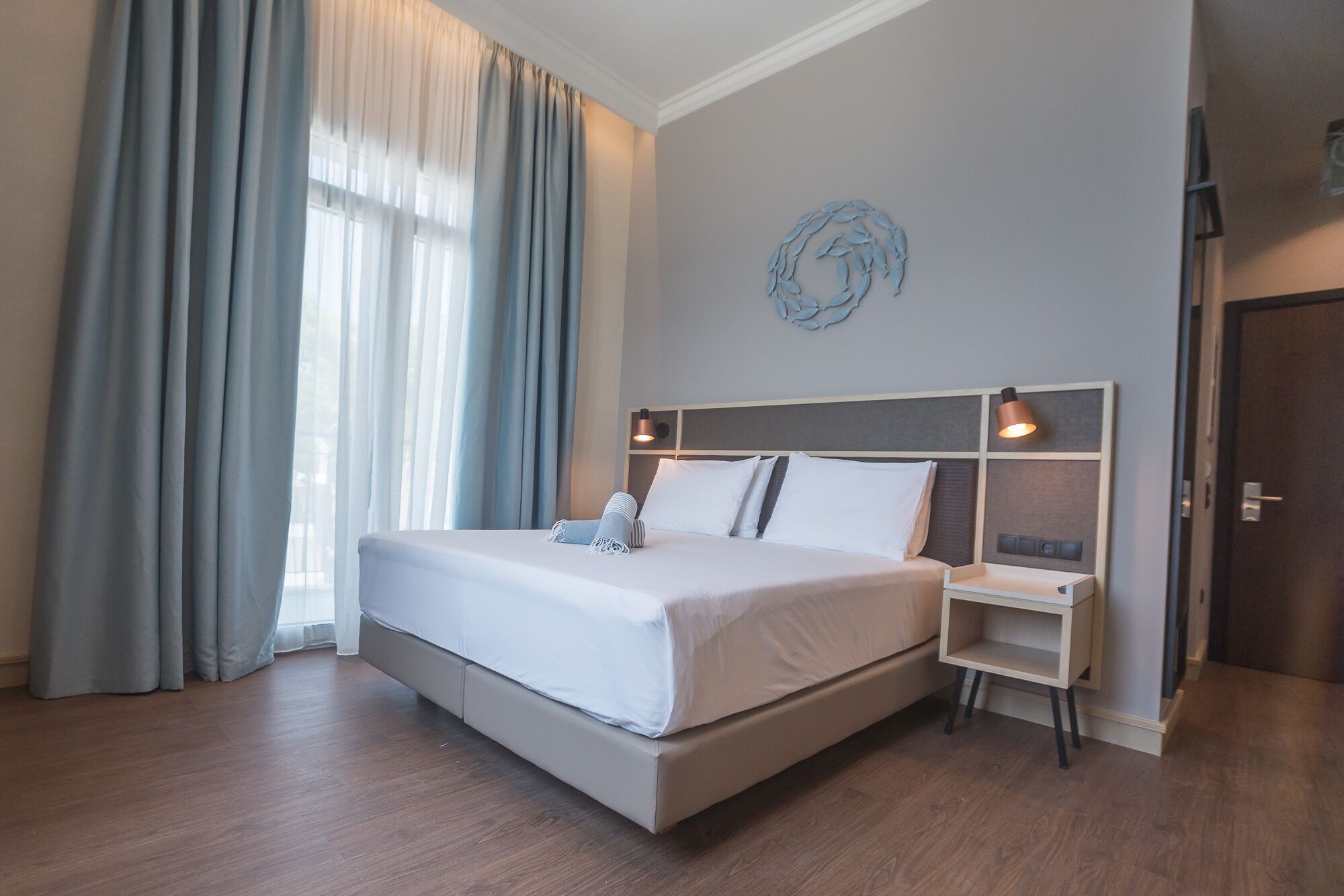 A modern hotel room with a large bed, a bedside table, and a small shelf.