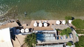 Vista aérea de una propiedad frente a la playa, con piscina, tumbonas y sombrillas.