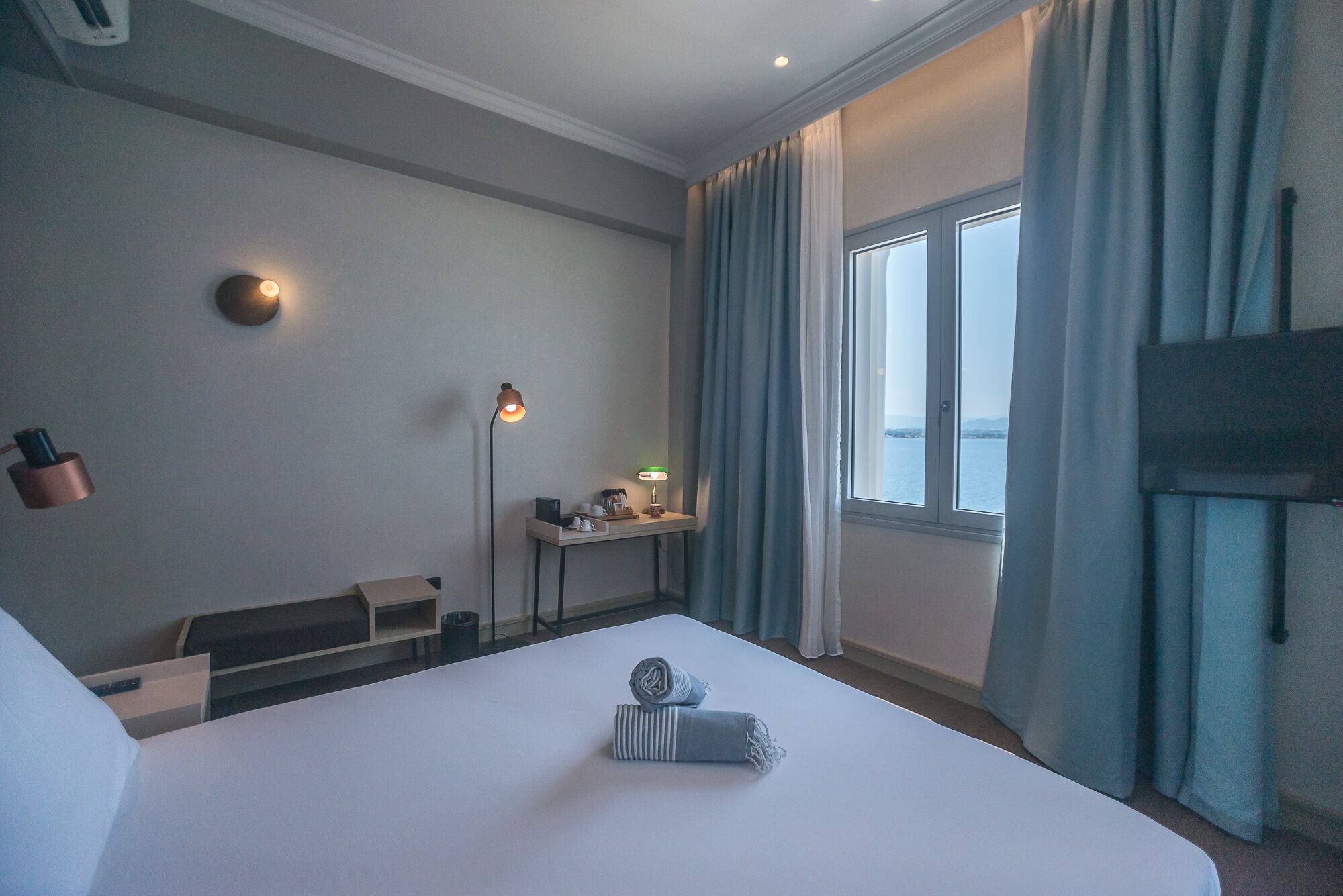 A hotel room with a bed, a desk, a lamp, and a TV.