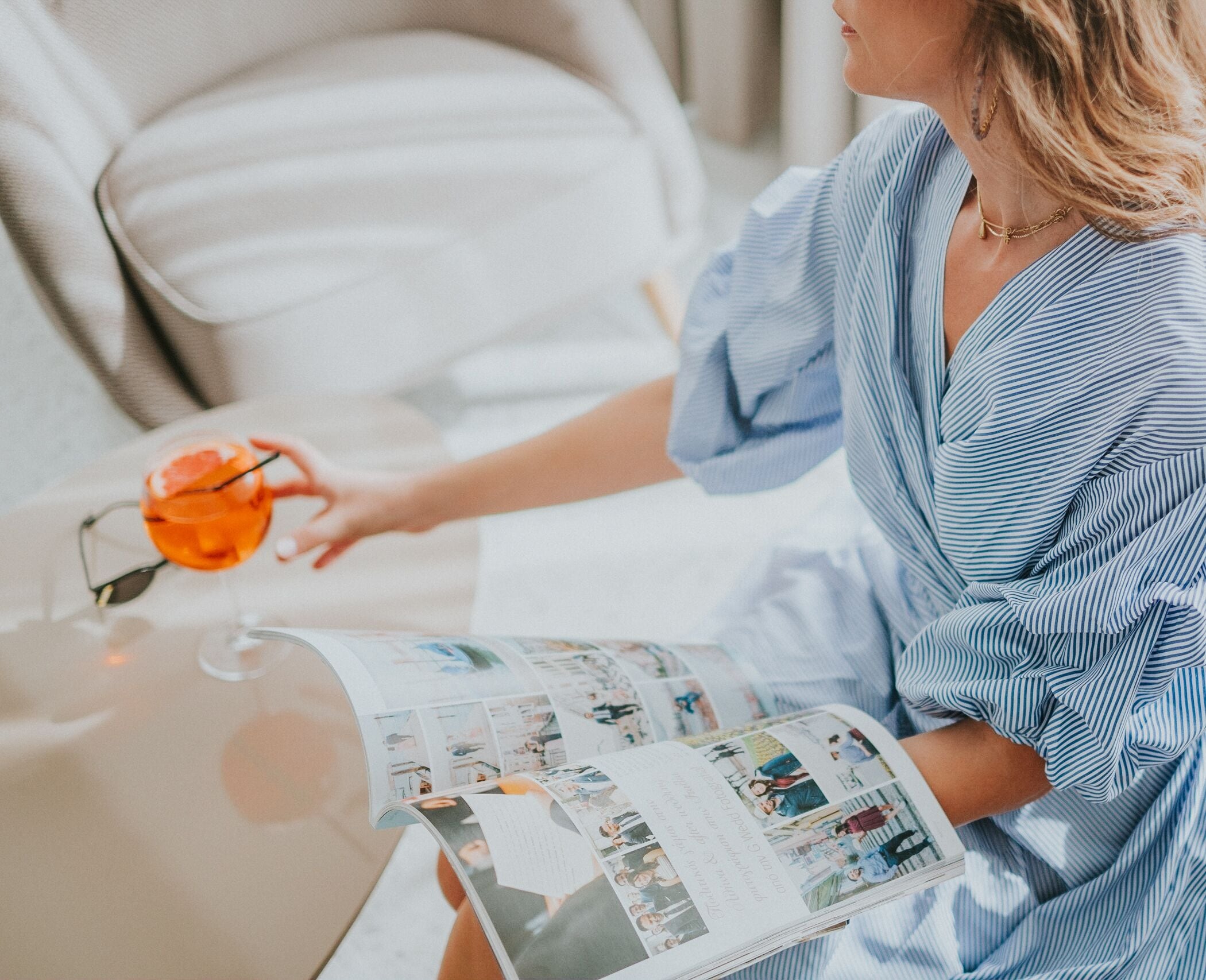A person sitting on a couch, holding a drink and reading a magazine.