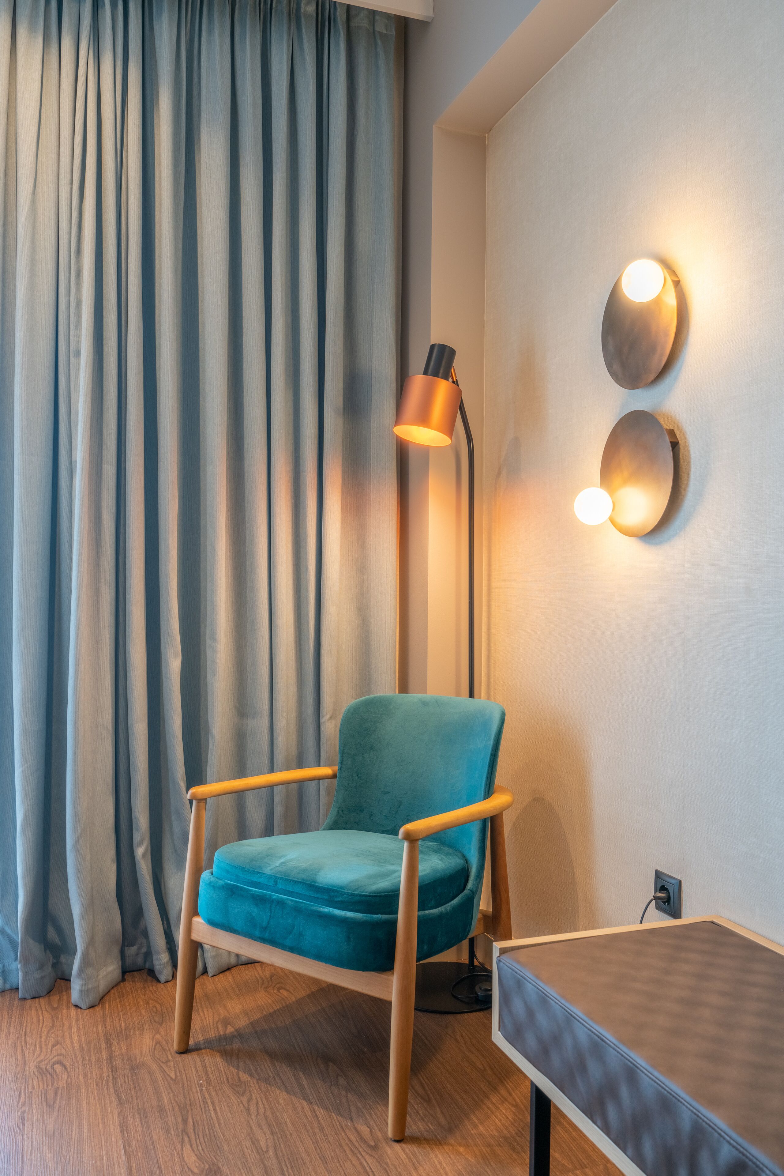 Ein Zimmer mit einem türkisfarbenen Ohrensessel, einer Stehlampe und einem Tisch.