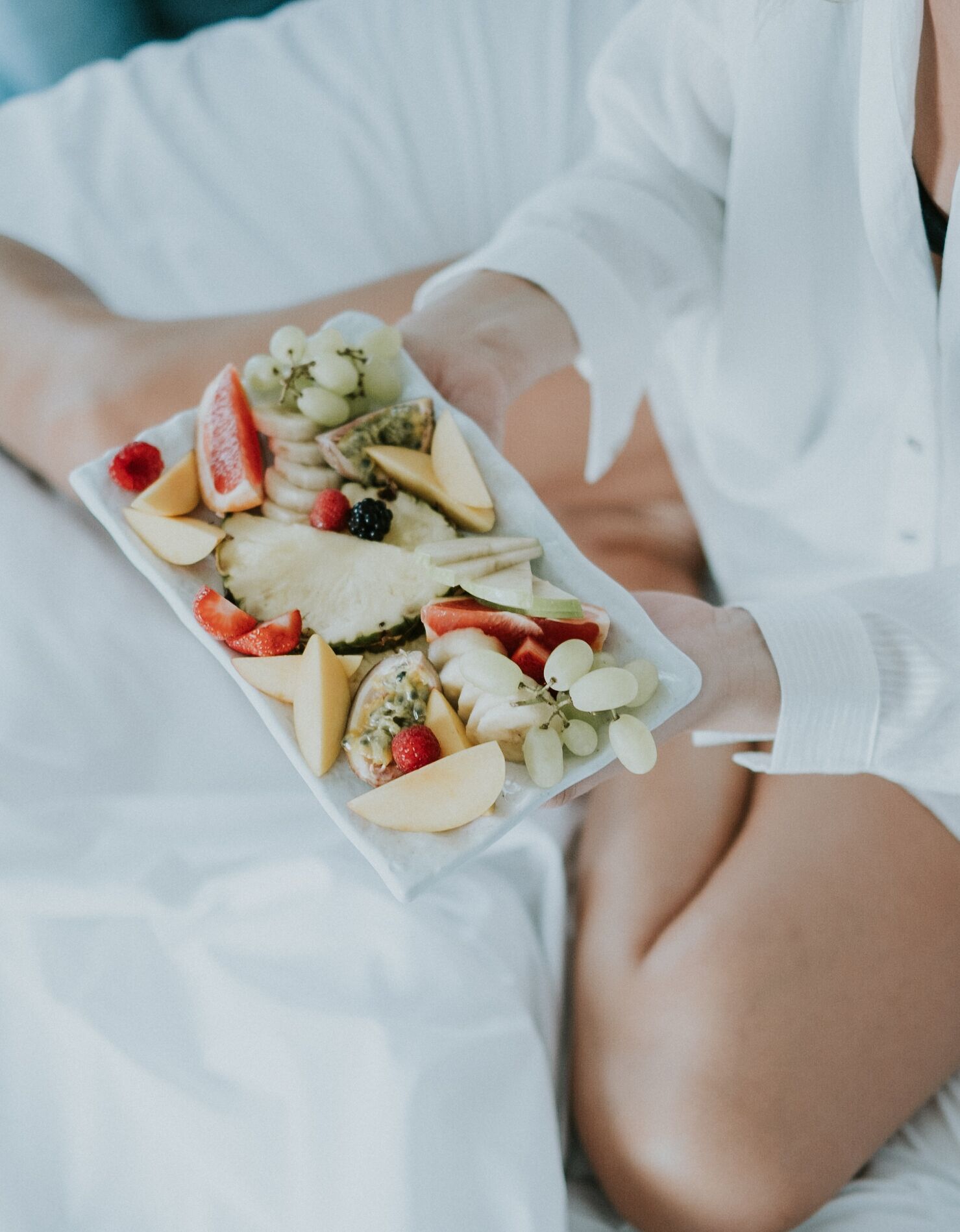 Una persona sosteniendo una bandeja rectangular blanca con frutas y queso.