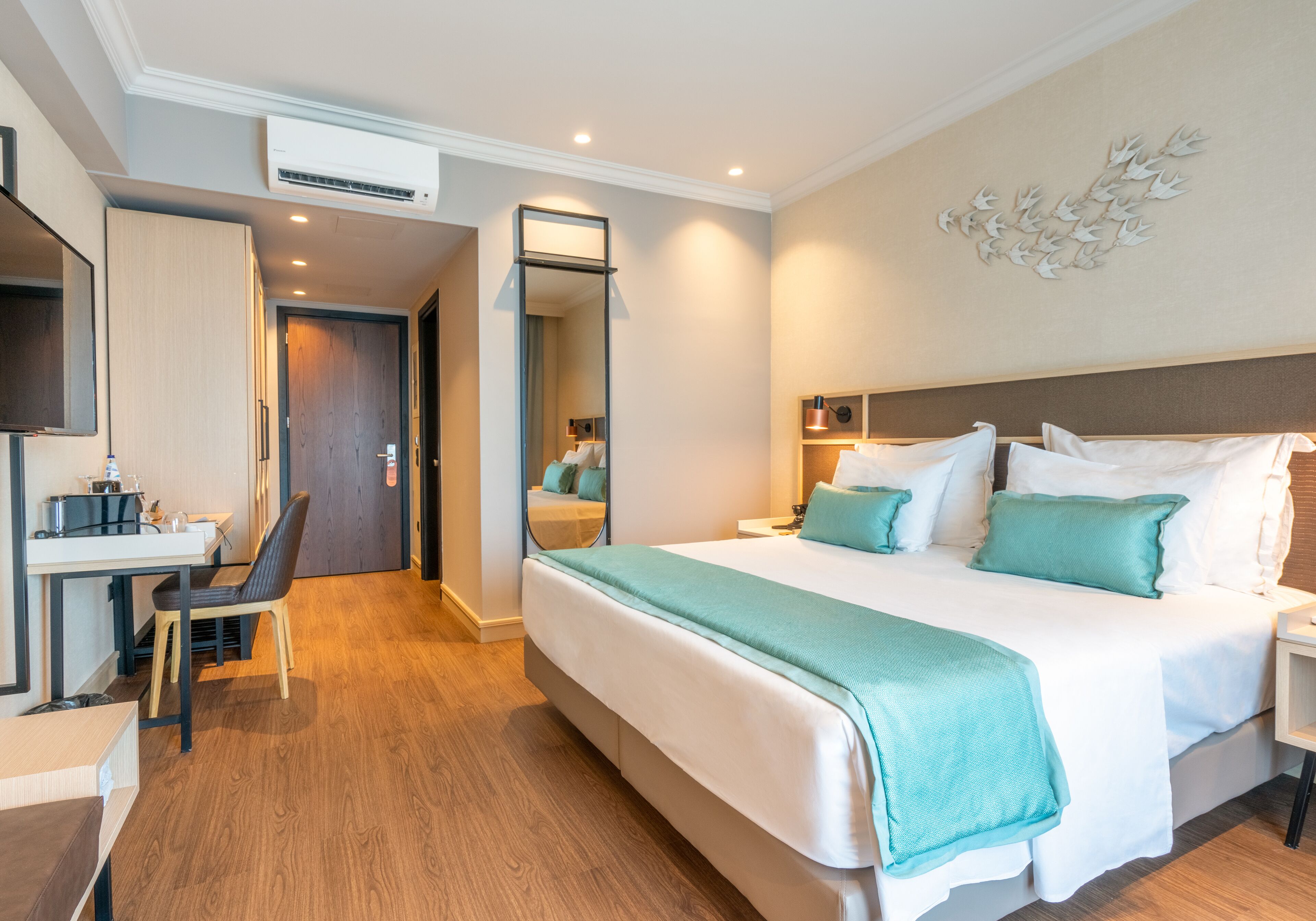 Habitació d'hotel amb un llit gran, un escriptori i una cadira. Hi ha un mirall a la paret i un aire condicionat de sostre.