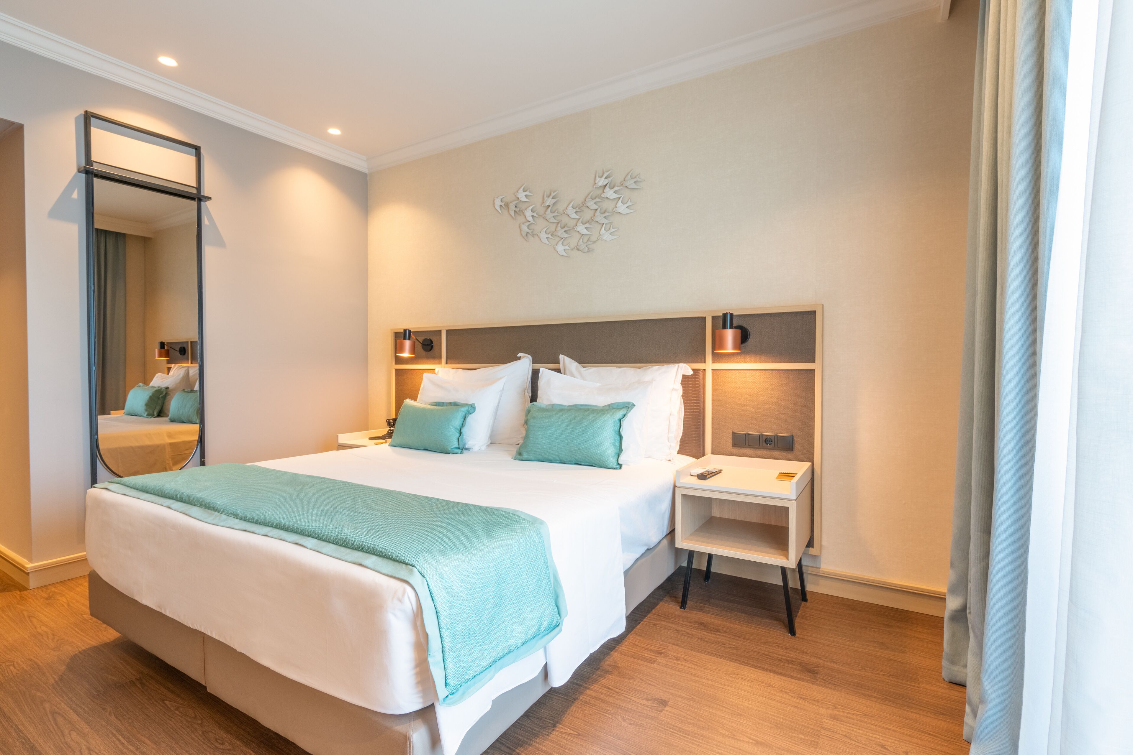 Una habitación de hotel moderna con una cama grande, mesitas de noche, un espejo y un adorno de pared.