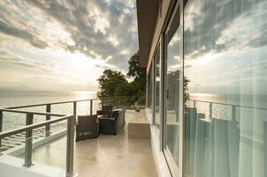 A balcony with a view of the sea and mountains, furnished with chairs and a table.