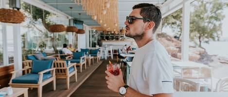 A man holding a drink in a restaurant with wooden furniture and large windows.