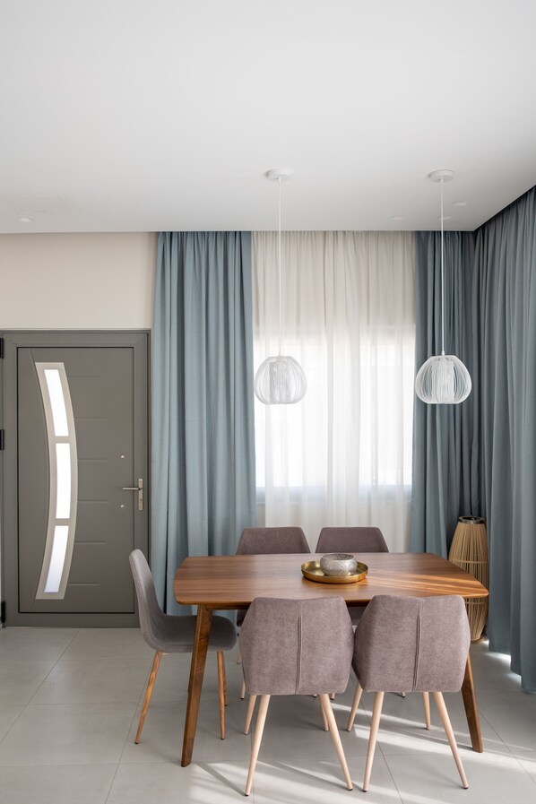 A modern dining area with a wooden table, six grey upholstered chairs, and two hanging pendant lights. - Pefkaki Boutique Hotel Loutraki (Loutraki-Agioi Theodoroi)