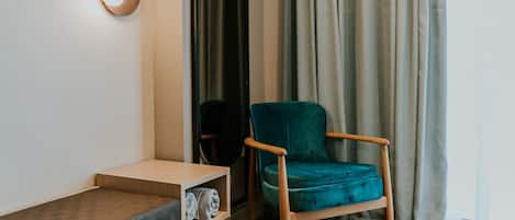 A modern room with a wooden floor, a teal armchair, a small wooden table, and a wall-mounted light fixture.