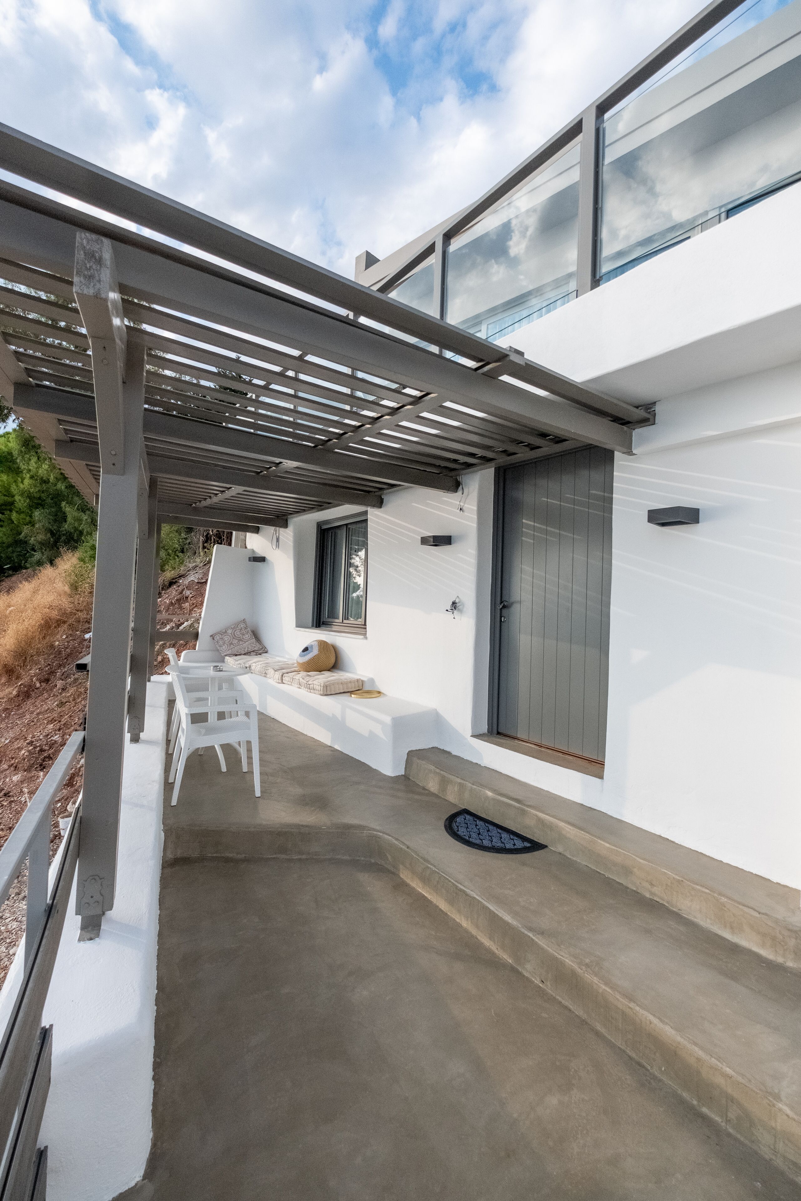 Et moderne hus med en overdækket terrasse, hvid facade og en grå dør.