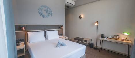 A hotel room with a bed, bedside tables, a desk, a lamp, and a wall-mounted air conditioner.