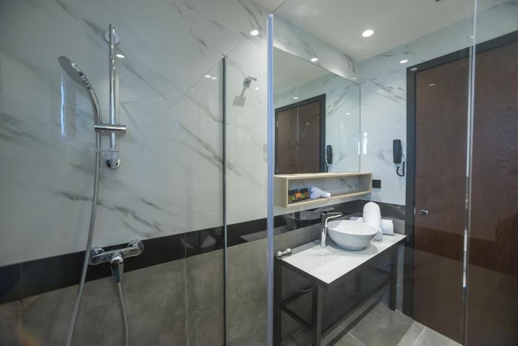 A modern bathroom with a glass-enclosed shower, a white sink, and a marble-tiled wall.