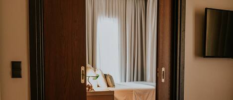 A hotel room with a wooden floor, a bed with white linens, a desk with a lamp, and a TV on the wall.