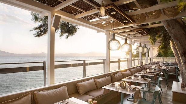 Un restaurante frente al mar con terraza, mesas y lámparas colgantes.