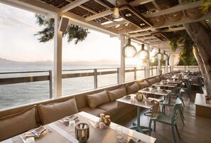 Ein Restaurant am Meer mit Terrassensitzgelegenheiten, Tischen und hängenden Leuchten.