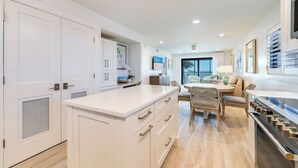 A modern kitchen with white cabinetry, a dining area with wicker chairs, and a large window. - OCEAN'S REACH 3A4: 2-Bdrm, Top Floor/Corner Unit, Stunning Views! (Sanibel Island)