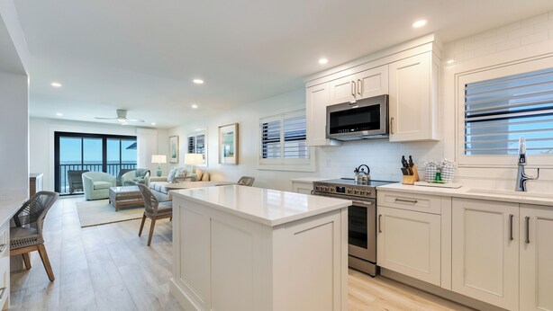 A modern kitchen with white cabinetry, a built-in microwave, and an oven. There is a dining area with a light-colored sofa and a coffee table. - OCEAN'S REACH 3A4: 2-Bdrm, Top Floor/Corner Unit, Stunning Views! (Sanibel Island)