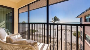 A balcony with a view of a beach, wicker furniture, and a railing. - OCEAN'S REACH 3A4: 2-Bdrm, Top Floor/Corner Unit, Stunning Views! (Sanibel Island)