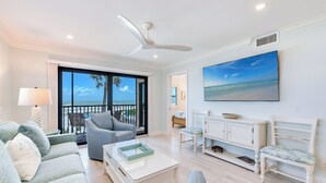 A spacious living room with a large TV, comfortable seating, and a balcony with a view of the ocean. - OCEAN'S REACH 2D2: 2-Bdrm, Corner/Gulf-Front View, All Amenities Open! (Sanibel Island)