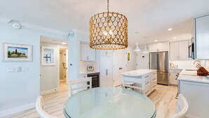 A modern kitchen with white cabinetry, a stainless steel refrigerator, and a glass dining table. - OCEAN'S REACH 2D2: 2-Bdrm, Corner/Gulf-Front View, All Amenities Open! (Sanibel Island)