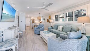 A spacious living room with a large TV, a ceiling fan, and a view of the kitchen. - OCEAN'S REACH 2D2: 2-Bdrm, Corner/Gulf-Front View, All Amenities Open! (Sanibel Island)