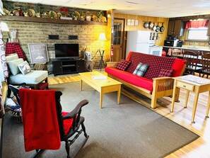 Una sala de estar acogedora con un sofá rojo, una televisión, una chimenea y una cocina visible a través de un umbral abierto.