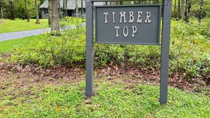 Un panneau indiquant « TIMBER TOP » dans une zone boisée, avec un bâtiment en arrière-plan.