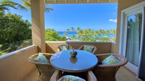 Ein Balkon mit Korbmöbeln und einem Glastisch, mit Blick auf einen Strand mit Palmen und dem Meer.