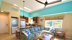 Eine moderne Küche mit Einbauofen und Mikrowelle, ein Essbereich mit Holztisch und Stühlen sowie ein Wohnzimmer mit gemustertem Sofa und Deckenventilator.