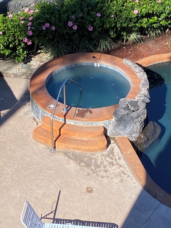 Un jacuzzi con borde de piedra, una escalera metálica y una repisa de piedra.