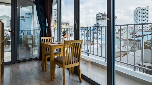 A balcony with a wooden table and chairs, large windows, and a view of the cityscape. - HAPPYHOMES 102 Luxury Bui Vien Apartment (Ho Chi Minh City)