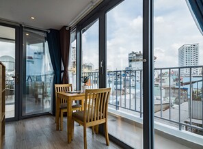 A balcony with a wooden table and chairs, large windows, and a view of the cityscape. - HAPPYHOMES 102 Luxury Bui Vien Apartment (Ho Chi Minh City)