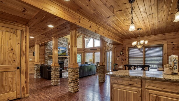 A spacious log cabin interior with a kitchen, dining area, and stone pillars. - Spacious 4BR Cabin w/ Indoor Pool, Hot Tub, Game Room & Mountain Views (Sevierville)