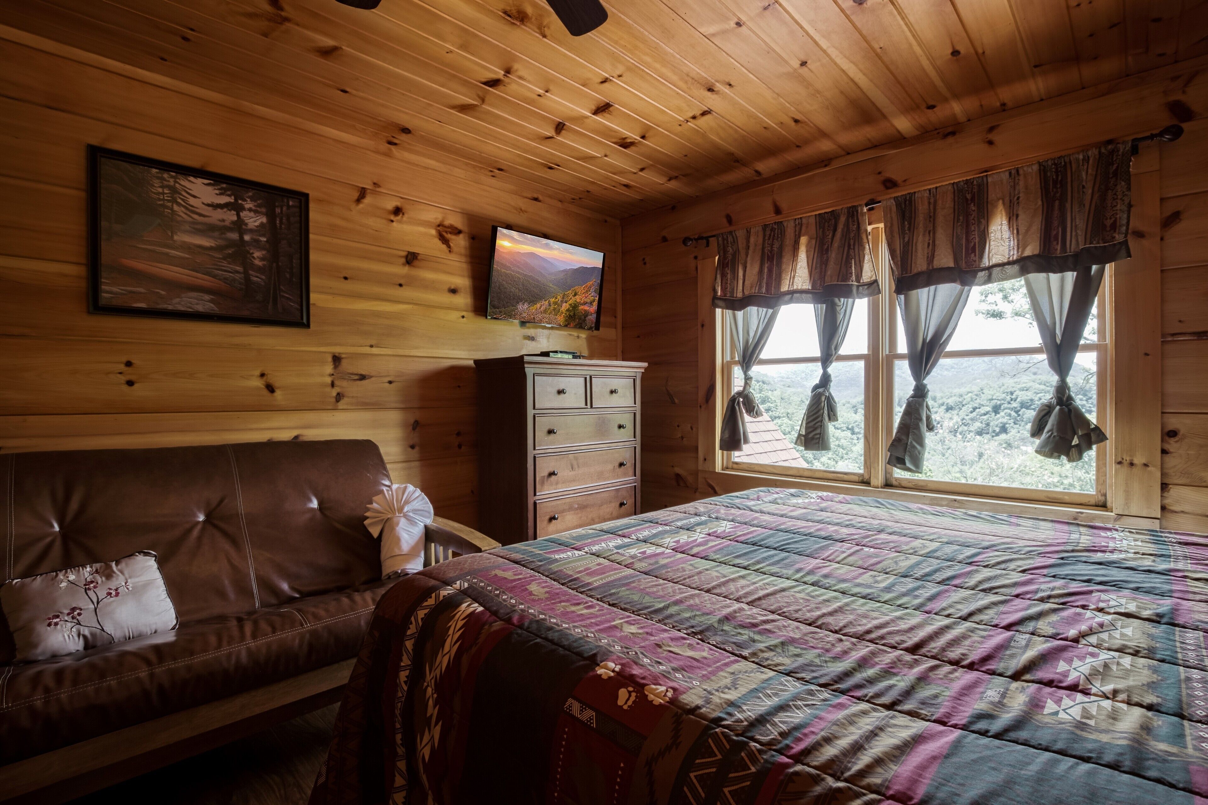 Ein Schlafzimmer einer Holzhütte mit einem Bett, einer Kommode, einem Sofa und einem Fenster mit Vorhängen.