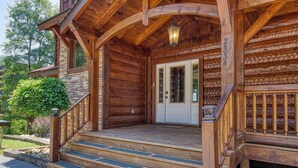 A wooden cabin with a stone foundation, a front porch with steps, and a double door. - Spacious 4BR Cabin w/ Indoor Pool, Hot Tub, Game Room & Mountain Views (Sevierville)