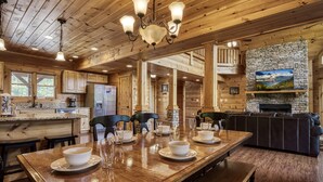 A wooden cabin interior with a dining table set for four, a fireplace, and a stone wall. - Spacious 4BR Cabin w/ Indoor Pool, Hot Tub, Game Room & Mountain Views (Sevierville)
