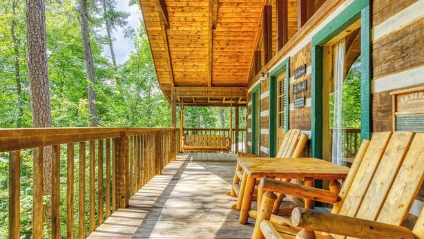 A wooden deck with benches and a covered area, surrounded by trees.