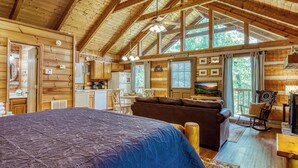 A log cabin interior with a large bed, a sofa, a dining area, and a kitchen.