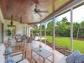 Relax in a spacious indoor area with a high ceiling and ceiling fan, surrounded by comfortable seating and a view of the lush garden.
