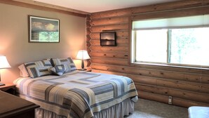 Quarto com parede de madeira, uma janela grande, cama com roupa de cama listrada, duas luminárias de cabeceira e um quadro na parede.