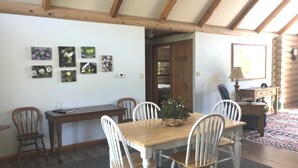 Uma área de refeições com mesa de madeira e cadeiras brancas, cercada por uma parede de madeira com arte floral.