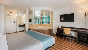 A hotel room with a bed, a desk, a chair, a TV, a bathroom with a bathtub, and a mirror.